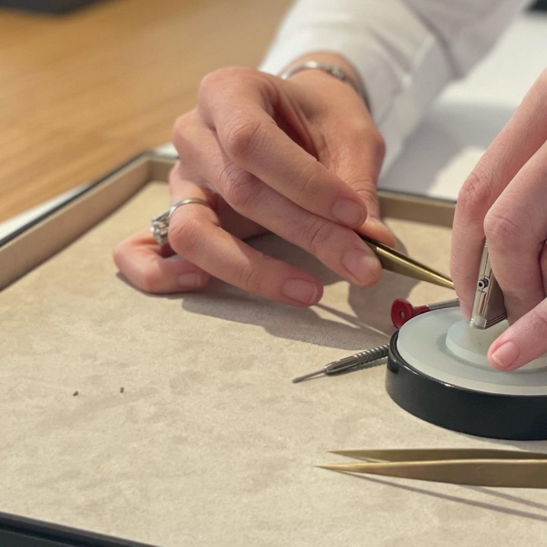 Hands carefully working on a rectangular metal watch case with tweezers and tiny screws.