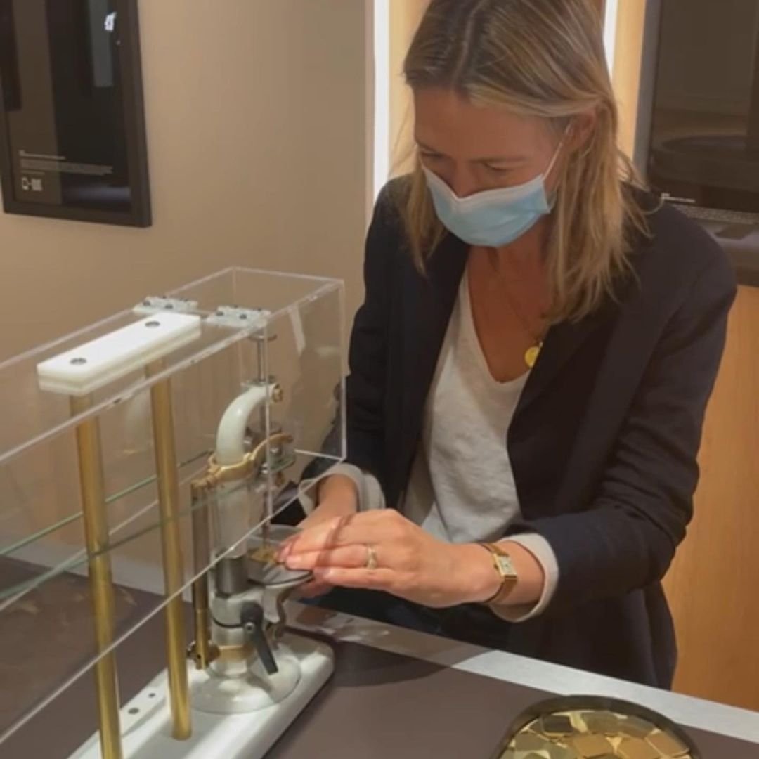 Francesca Cartier Brickell, masked, uses a clear acrylic machine to press small gold pieces.