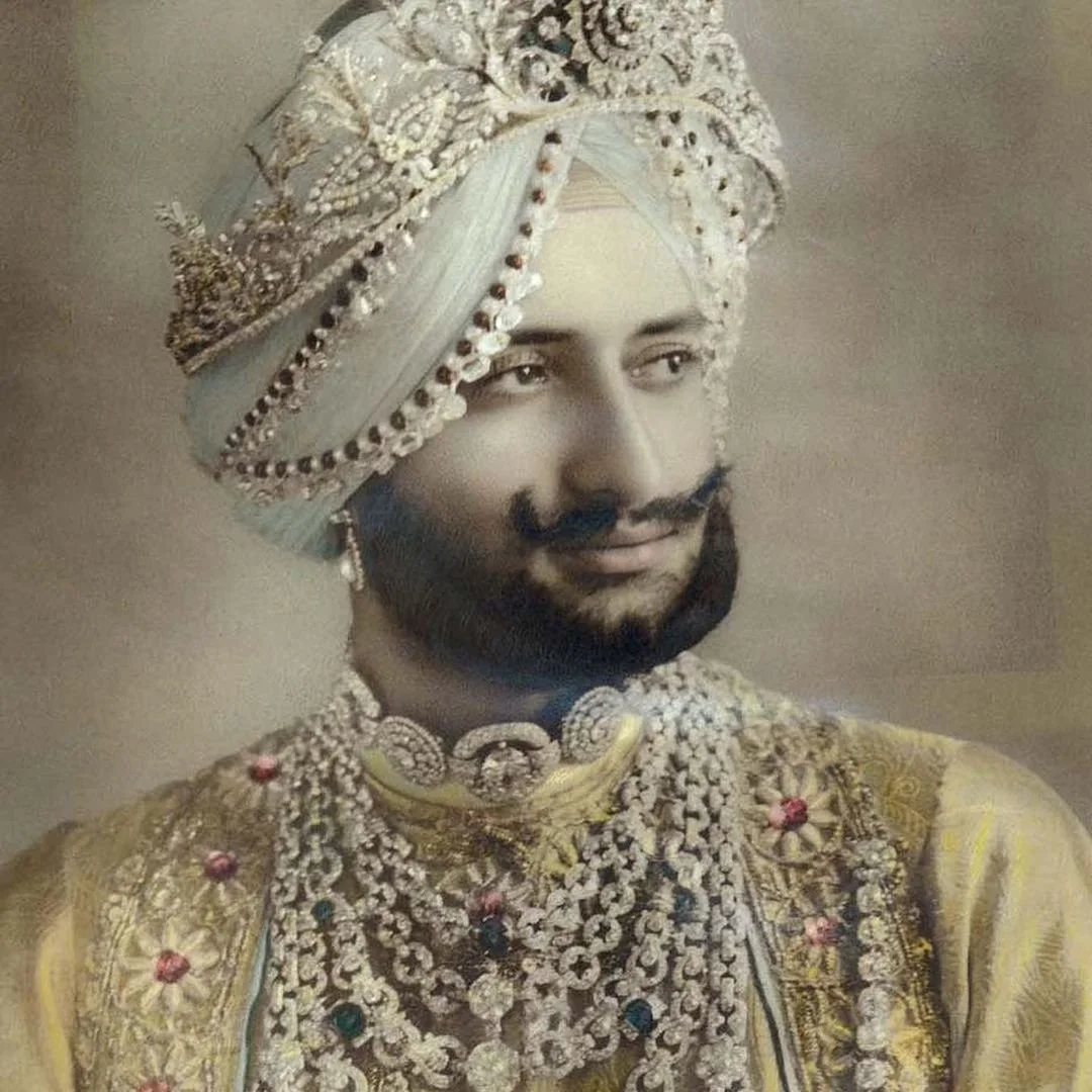 Regal man in a blue turban and golden robe, adorned with elaborate diamond and gemstone jewellery.