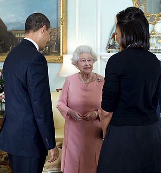 Queen Elizabeth II in pink, wearing a pearl necklace and brooch, smiles between the Obamas.