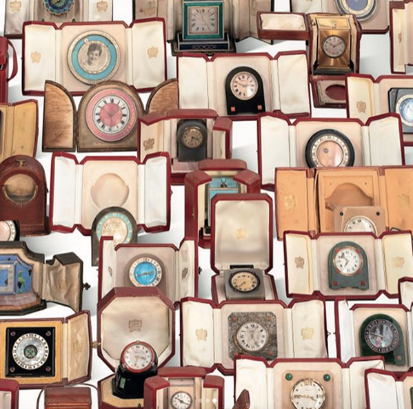 Many vintage Cartier clocks, varied designs, displayed in open red leather presentation boxes.