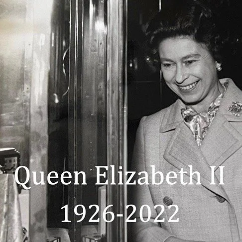 Smiling Queen Elizabeth II in a coat, wearing pearl earrings and a diamond brooch.