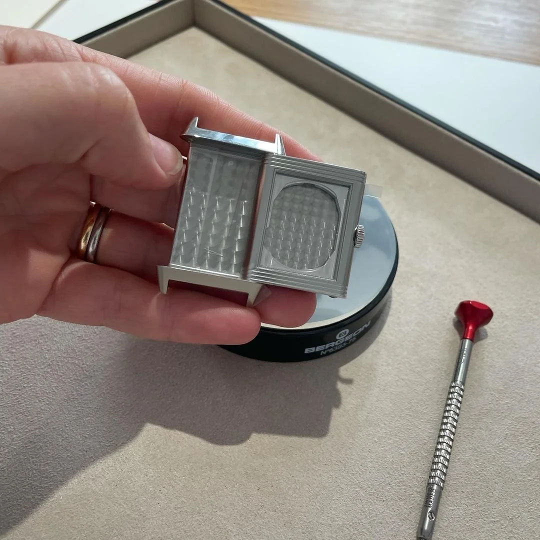Hand holds an open silver rectangular watch case with engine-turned patterns.