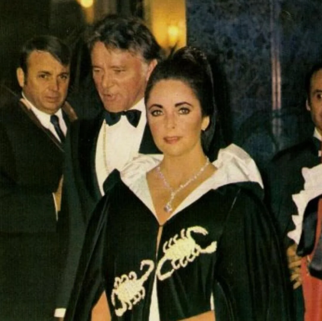 Elizabeth Taylor in a diamond necklace and scorpion-embroidered cape with Richard Burton.