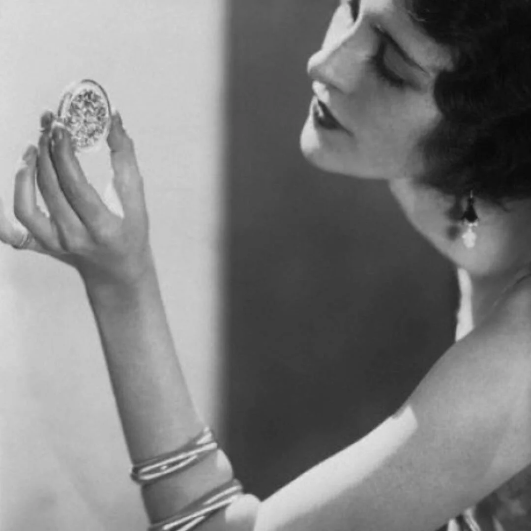 1920s woman in profile, admiring a diamond-set compact, wearing bangles and a drop earring.