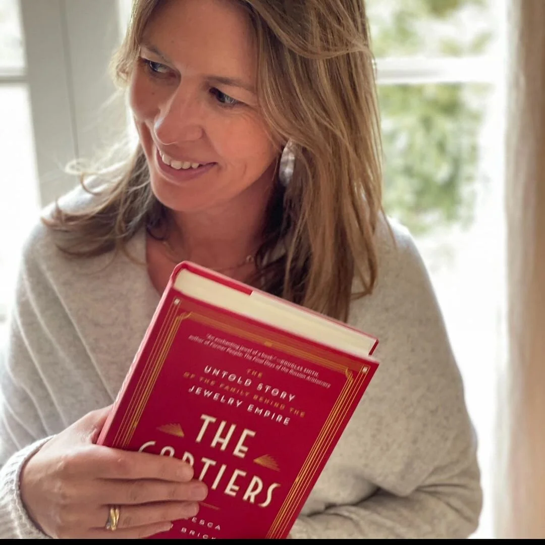 Francesca Cartier Brickell smiles, holding her red book, "The Cartiers," with gold lettering.