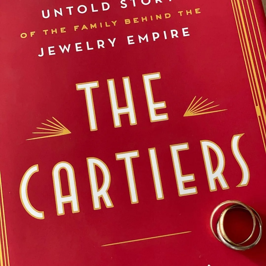 Red book cover "The Cartiers" with a classic yellow, white, and rose gold Trinity ring.