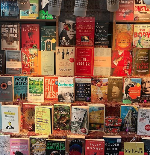 A bookshop window display filled with many books, including "The Cartiers.